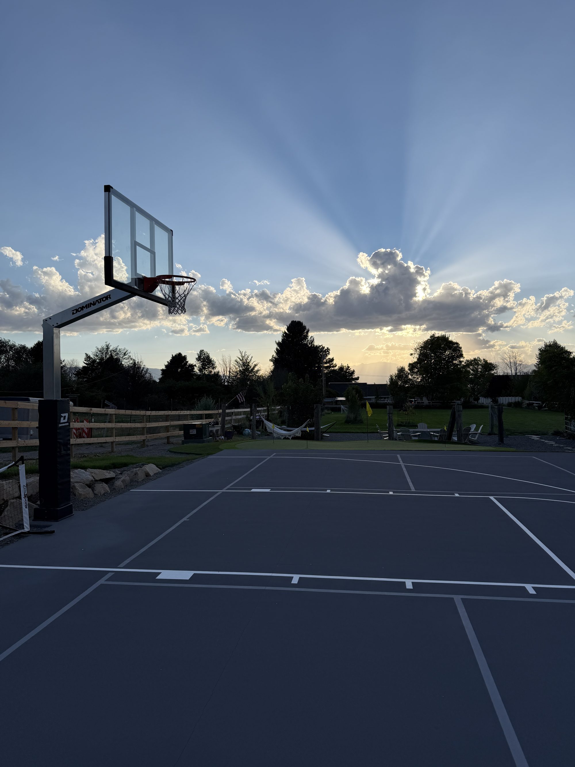 A backyard sport court at sunset in Utah, with a putting green, hammocks, and a fire pit behind it