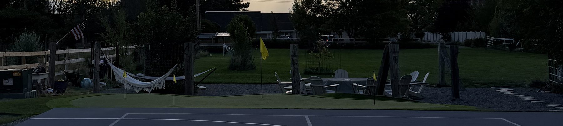 Wide view of the yard: putting green, hammocks, fire pit seating, and lawn at dusk
